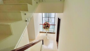 A modern staircase with glass railings and a polished floor leading to a room with a large window and a vase of flowers.