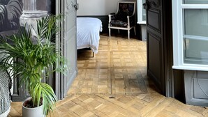 Ett rum med en säng, en stol, ett inramat porträtt och en stor målning på väggen.