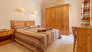 Une chambre à coucher avec un lit en bois, deux tables de chevet, une armoire et un bureau.