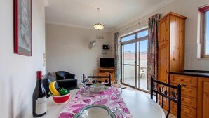 Un coin repas avec une table dressée pour deux personnes, une bouteille de vin et un saladier de fruits.