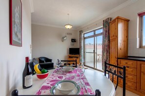 Un coin repas avec une table dressée pour deux personnes, une bouteille de vin et un saladier de fruits.