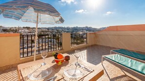 Une terrasse avec une table dressée pour deux personnes, un parasol à rayures et une vue sur la ville.
