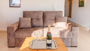 Un salon avec un canapé beige, une table basse en bois, une bouteille de champagne et deux verres.