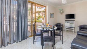 Un espace de vie comprenant une table à manger, des chaises, un canapé, un téléviseur et un balcon avec des rideaux.