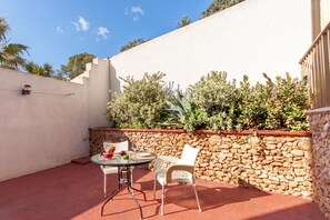 A patio with a round table and two chairs, a stone wall, and greenery.