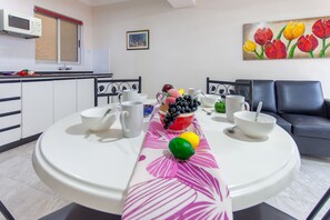 A dining area with a table set for two, a microwave, and a painting of tulips on the wall.