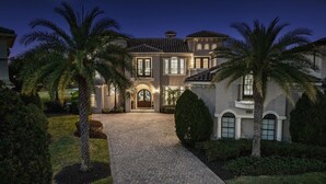 A large, two-story house with a paved driveway and palm trees. - Legends Palmer: Private Pool, Game Room, Theater, Gym, Free Water Park, Near Disney (Kissimmee)