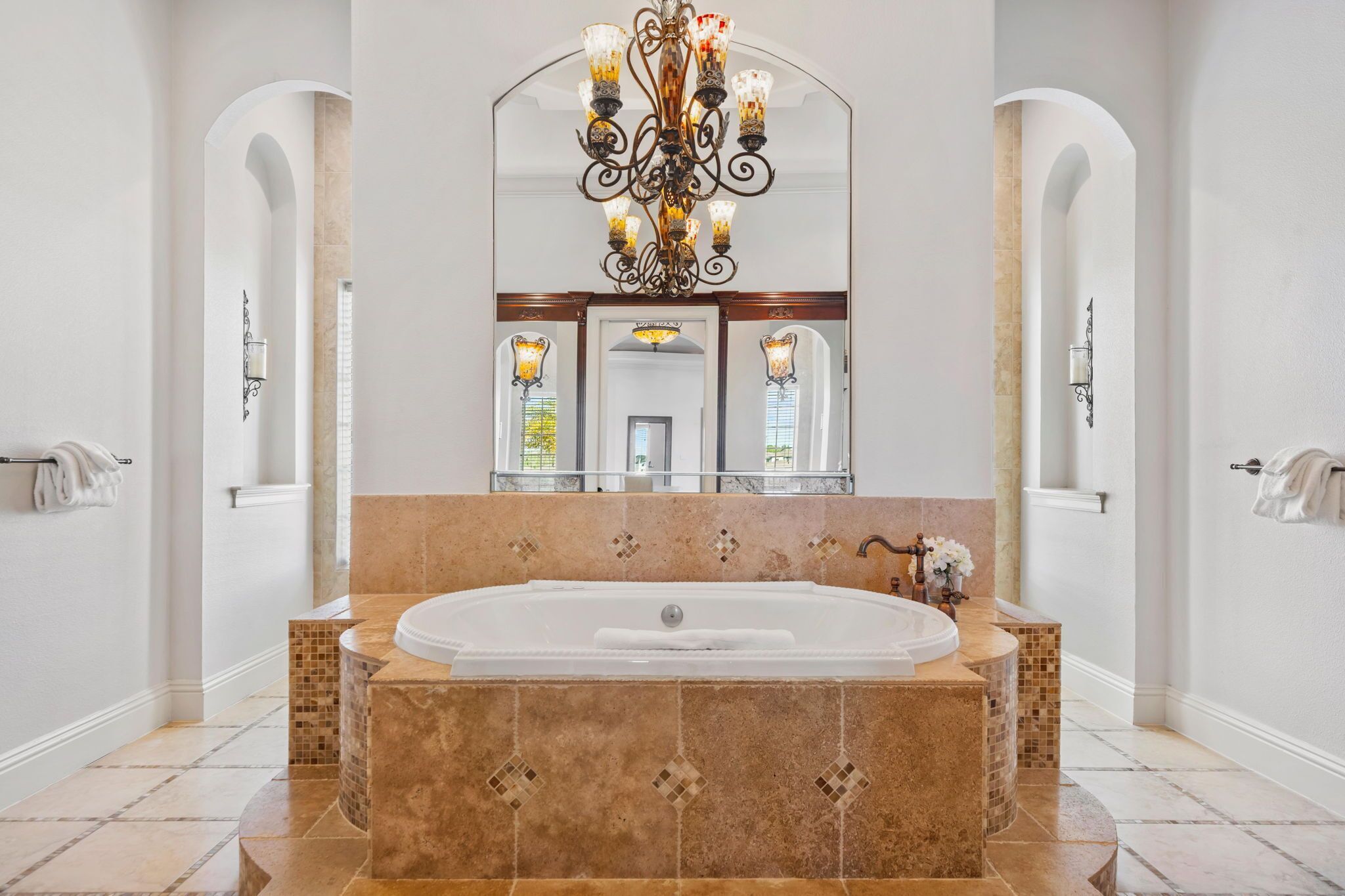 A spacious bathroom with a large bathtub, a decorative chandelier, and a mirrored wall.