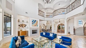 A spacious living room with a high ceiling, a fireplace, and a staircase leading to an upper level. - Legends Palmer: Private Pool, Game Room, Theater, Gym, Free Water Park, Near Disney (Kissimmee)