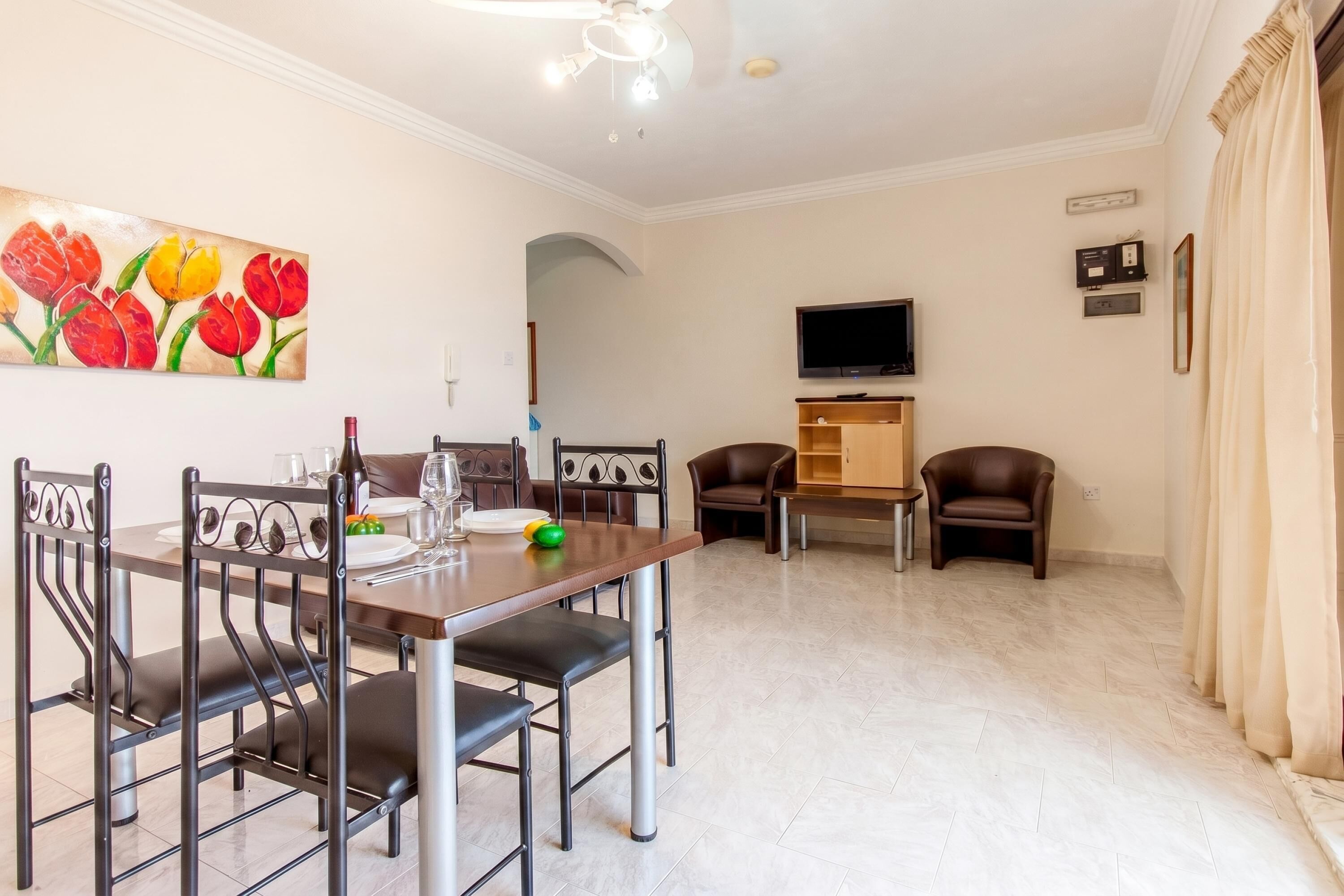 A dining area with a table, chairs, a painting, a television, and a cabinet.