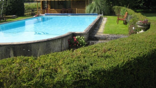 En swimmingpool med ett trädäck och ett hus med solpaneler i bakgrunden.