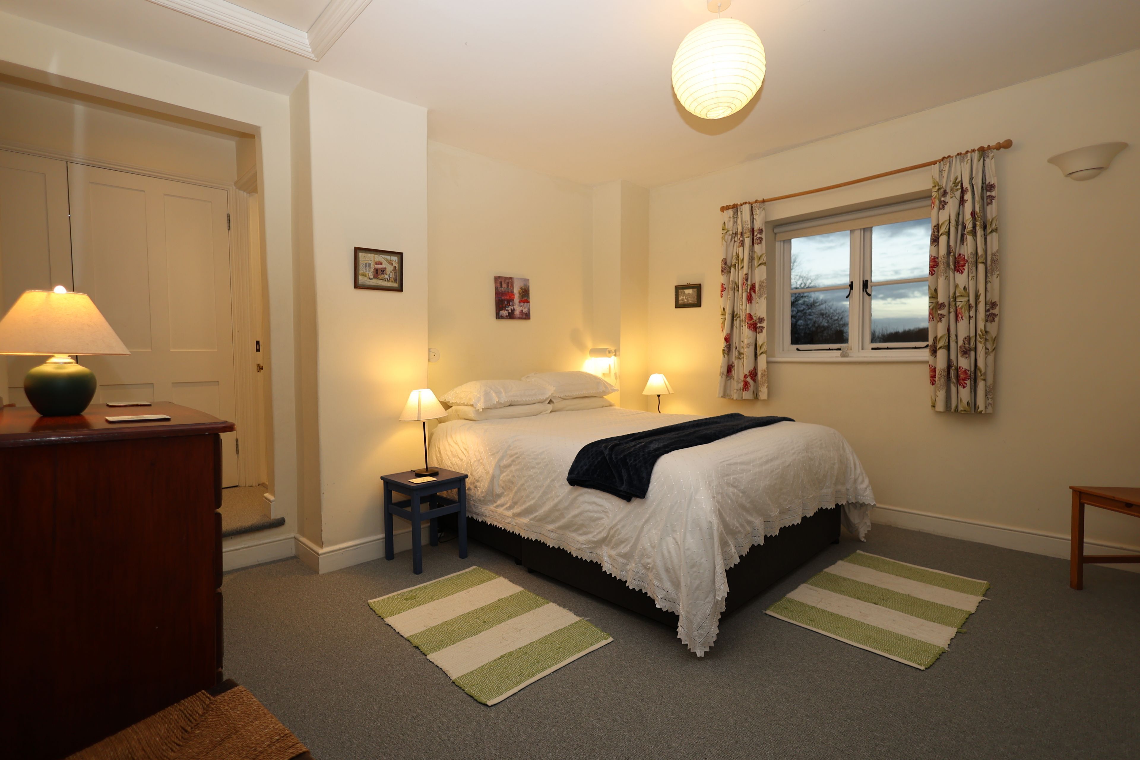 A bedroom with a bed, bedside lamps, a window with curtains, a dresser, and a rug.
