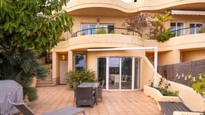 Un edificio residencial con patio que incluye una mesa, sillas, una tumbona y un espacio de estar techado.