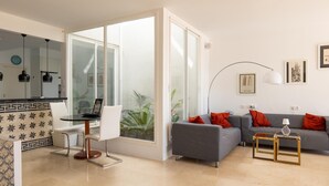 Una sala de estar moderna con un sofá, una mesa de comedor con sillas, un separador de vidrio y vistas al exterior.