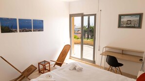Habitación de hotel con cama, escritorio, silla, vista de la ciudad y balcón.