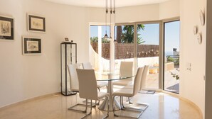 Un comedor moderno con una mesa y sillas de vidrio, obras de arte en las paredes y vistas al patio exterior.