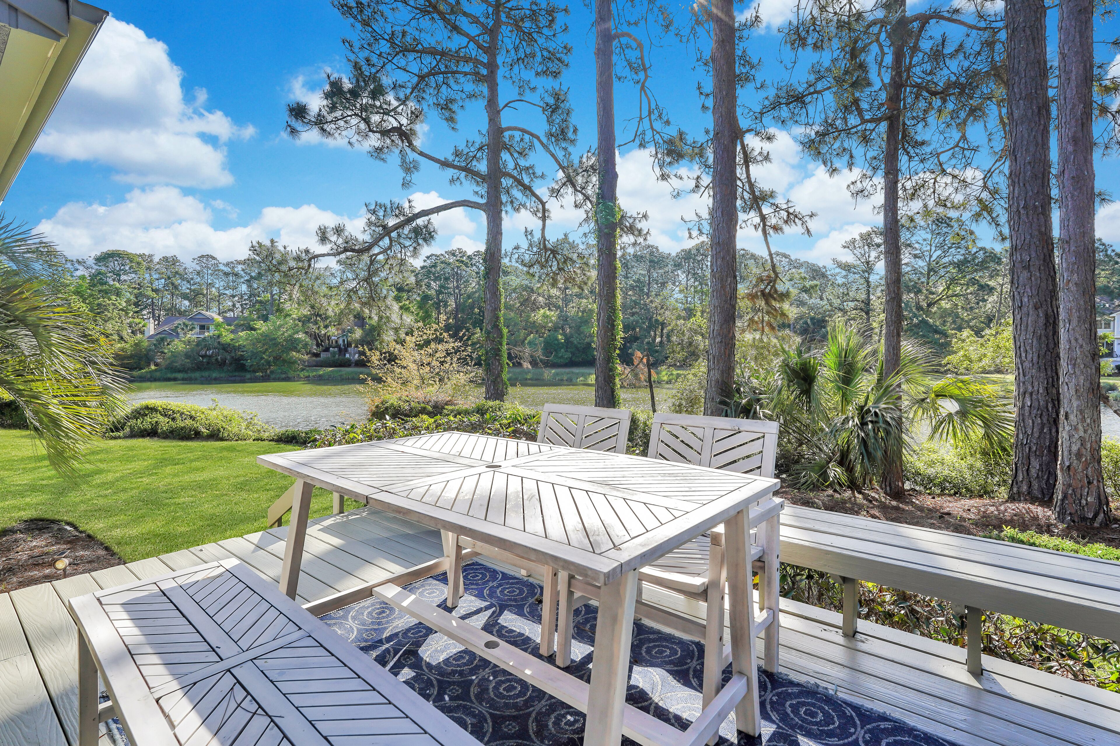 Une terrasse en bois avec une table et des bancs, entourée d’arbres et offrant une vue sur un lac.