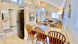 Una cocina amplia con una larga mesa de comedor y sillas de madera, un refrigerador y una ventana con vistas.