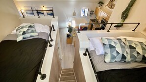 Una habitación tipo dormitorio con literas, una zona de cocina y una escalera.