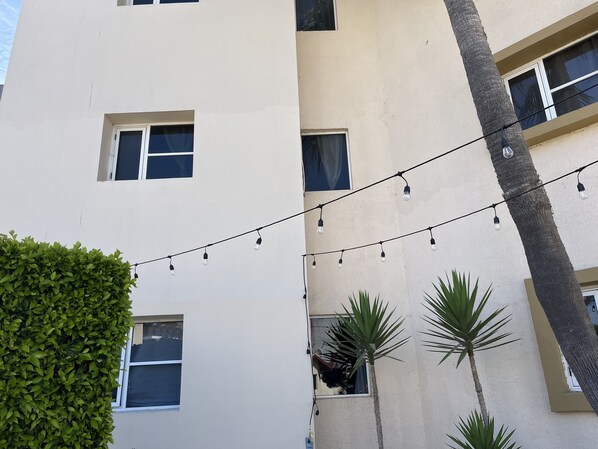 A building facade with multiple windows, string lights, and a palm tree. - Villa Serena Condo (Rosarito)