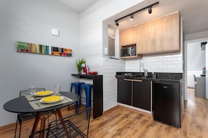 A compact kitchen with black appliances, a dining area with a table and chairs, and a small plant on the counter.