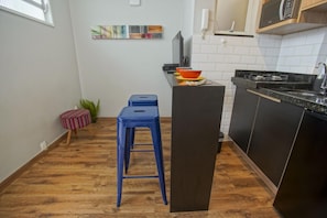 Une cuisine compacte avec un plancher en bois, un petit îlot avec des tabourets, un four à micro-ondes et un évier.