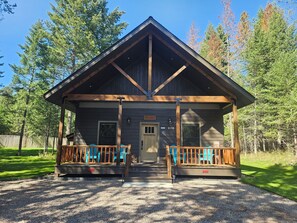 A lodge with a wooden exterior, a porch with blue chairs, and a gravel driveway.