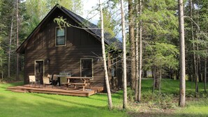A cabin with a deck, outdoor seating, and a grill.