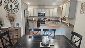 A modern kitchen with white cabinets, a black dining table, and a large wall clock.