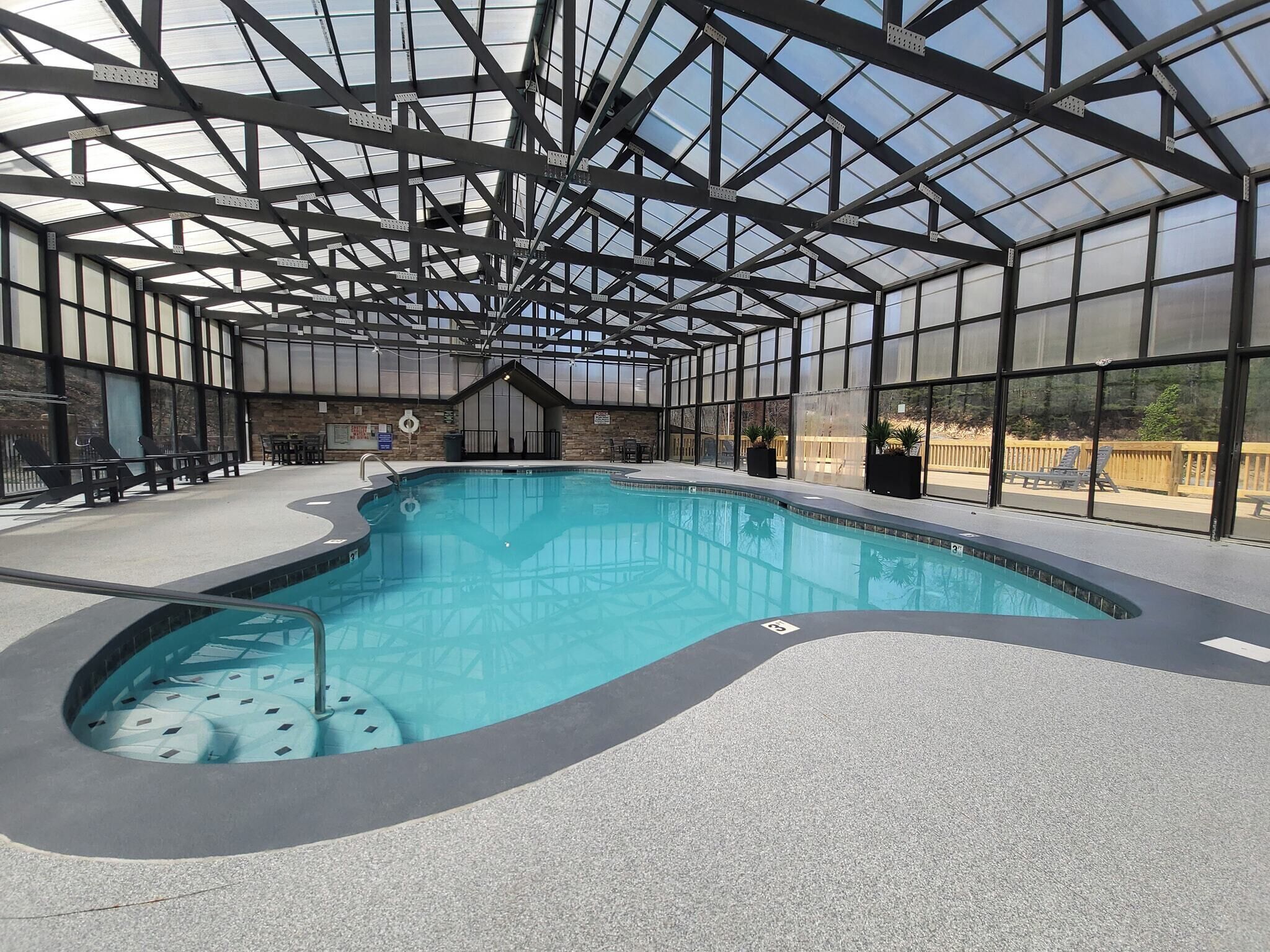 An indoor swimming pool with a glass ceiling, lounge chairs, and a stone wall.