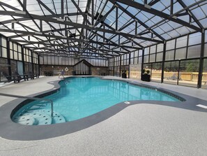 An indoor swimming pool with a glass ceiling, lounge chairs, and a stone wall. - Renovated Cabin. Hot tub, Arcade, Pool Table, Shuffle Board, Dollywood, Parking  (Sevierville)