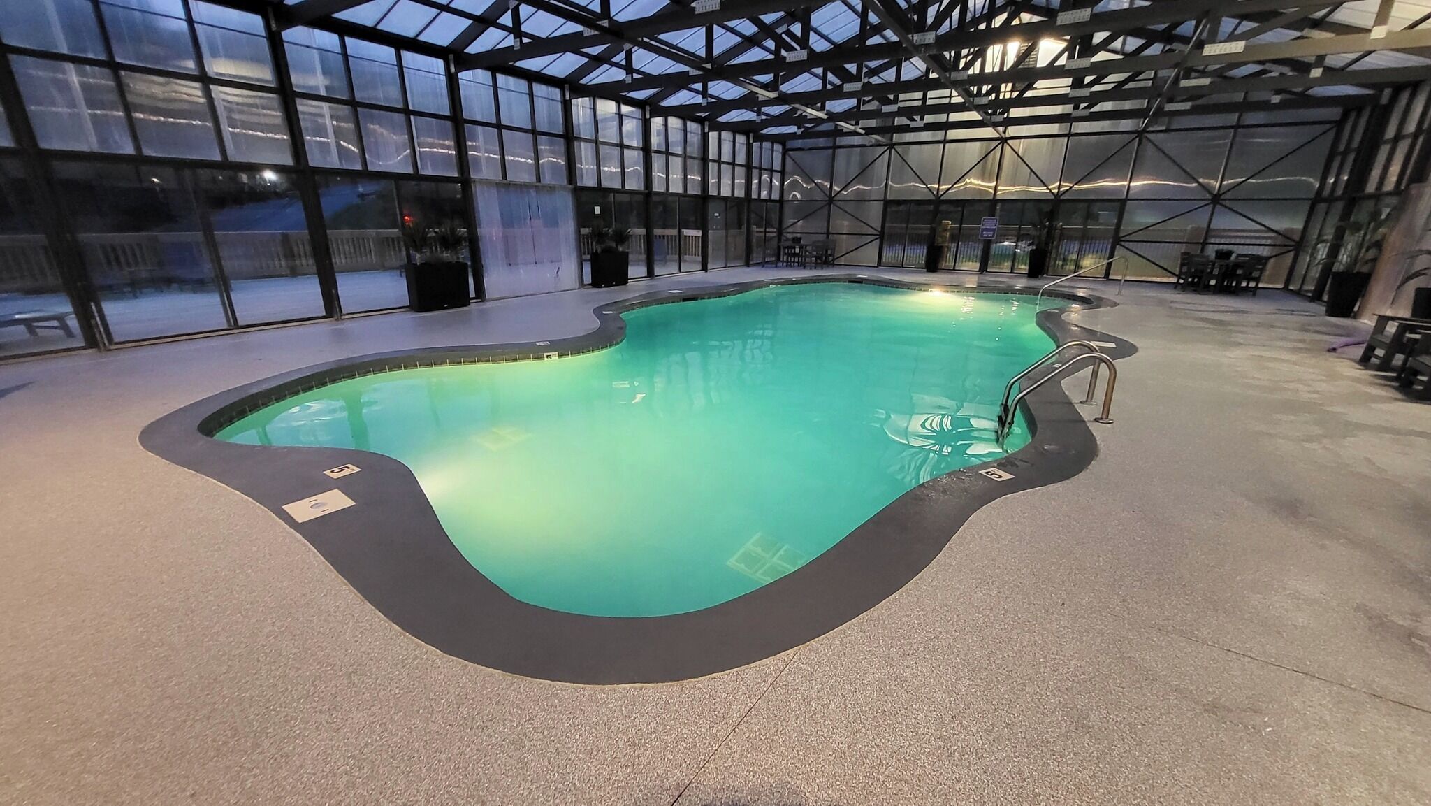 Una piscina interior de diseño curvo, rodeada por paredes de cristal y una estructura de techo metálico.