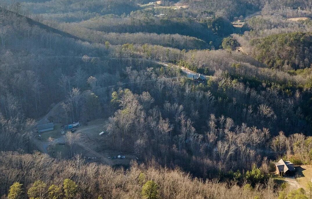 Vue aérienne d’une zone boisée avec un petit bâtiment et un chemin de terre.