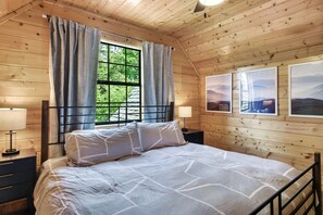 A wooden cabin bedroom with a bed, curtains, a window, and framed pictures on the wall. - Renovated Cabin. Hot tub, Arcade, Pool Table, Shuffle Board, Dollywood, Parking  (Sevierville)
