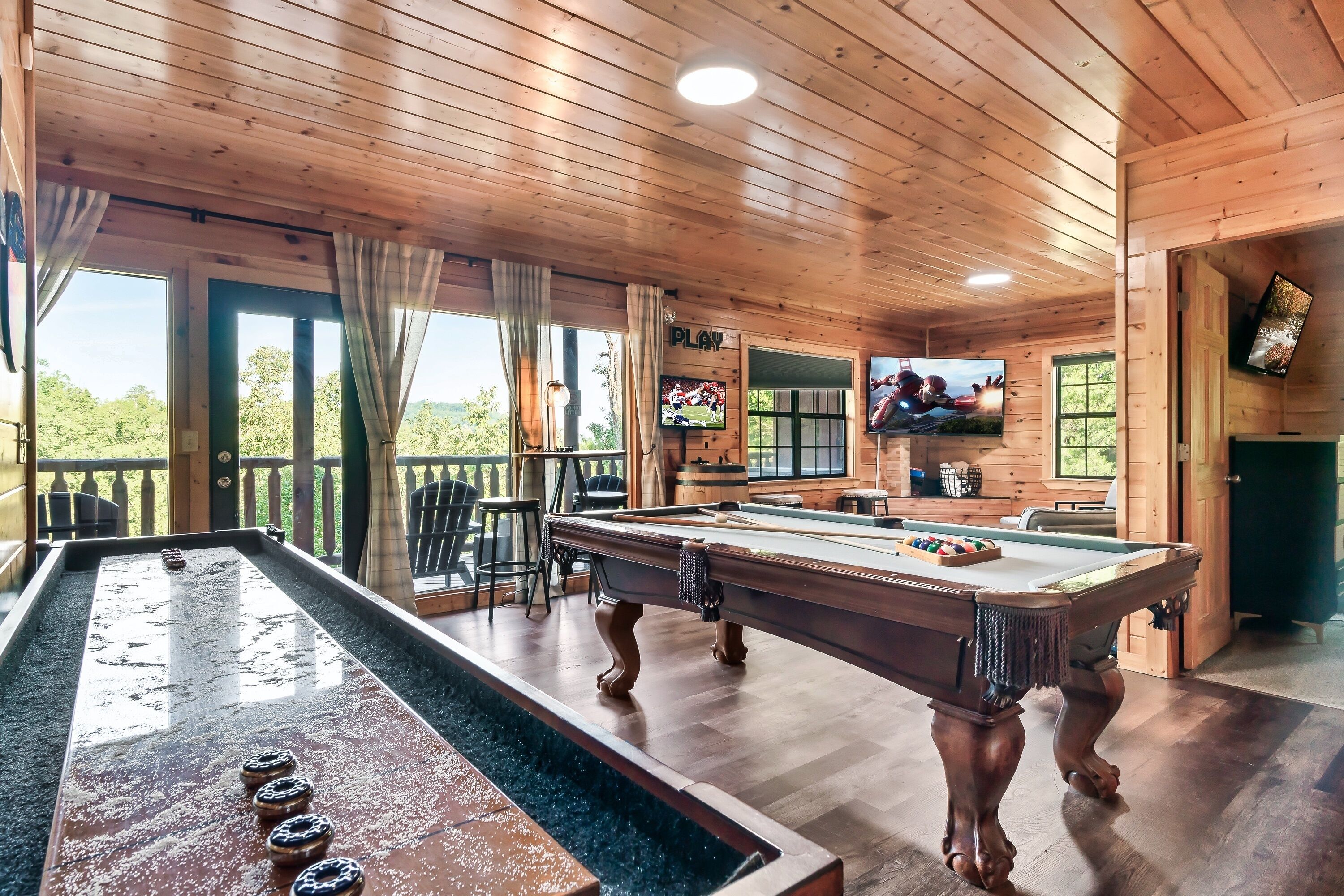 A wooden-paneled room with a pool table, two TVs, and a view of the outdoors.