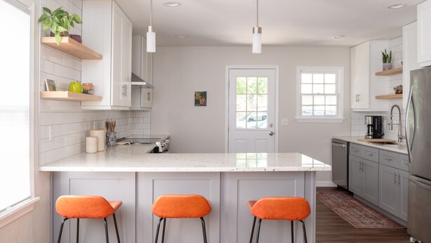 A modern kitchen with white cabinets, a central island with bar stools, pendant lighting, and a view of the outdoors.