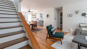 A staircase leading to a living area with a dining table, chairs, a sofa, and a kitchen in the background.