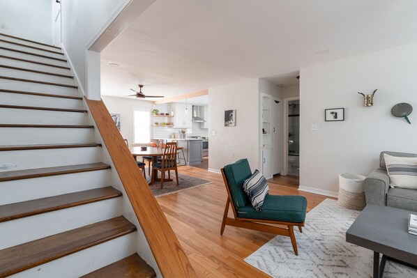 Una escalera conduce a un espacio de estar con una mesa de comedor, sillas, un sofá y una cocina al fondo.