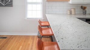 A modern kitchen with a white island, wooden stools, and a window.