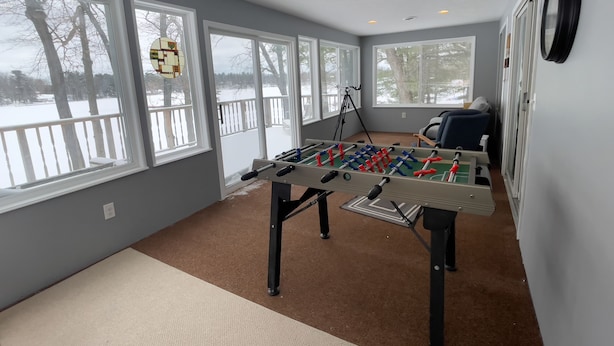 Una habitación con mesa de fútbol, ventanas amplias, un trípode y una silla.