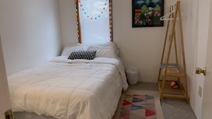 Un dormitorio con una cama, ventilador de techo, ventana con persianas, un cuadro, zapatero y alfombra.