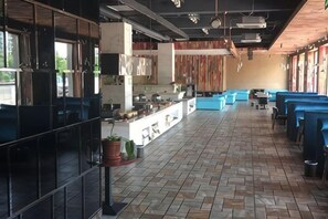 A spacious restaurant with a long counter, blue seating, and a tiled floor. - Xinhao Business Hotel (Yichun)