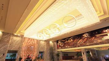 Un hall de hotel con suelo de mármol, una recepción y un gran cartel iluminado.
