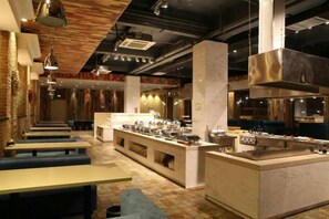 A restaurant interior with multiple seating areas, a central counter, and a visible kitchen area. - Xinhao Business Hotel (Yichun)