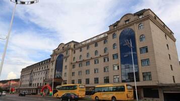 Un hotel de varios pisos con un gran arco central, numerosas ventanas y un estacionamiento con autobuses.
