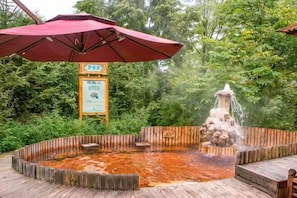 A hot spring area with a wooden deck, a red umbrella, and a signboard. - Xinhao Business Hotel (Yichun)