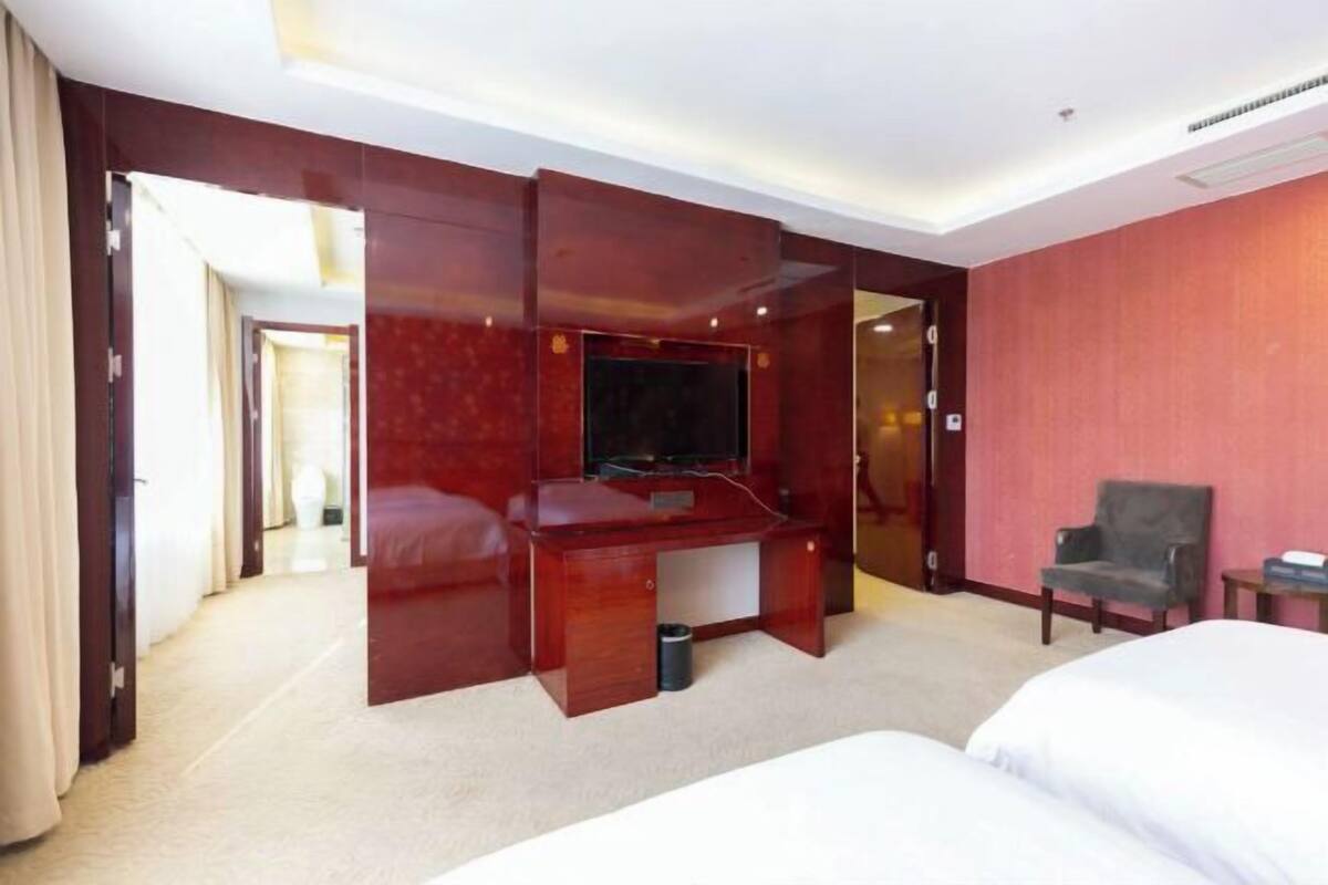 A hotel room with a large bed, a desk with a flat-screen TV, a chair, and a small table.