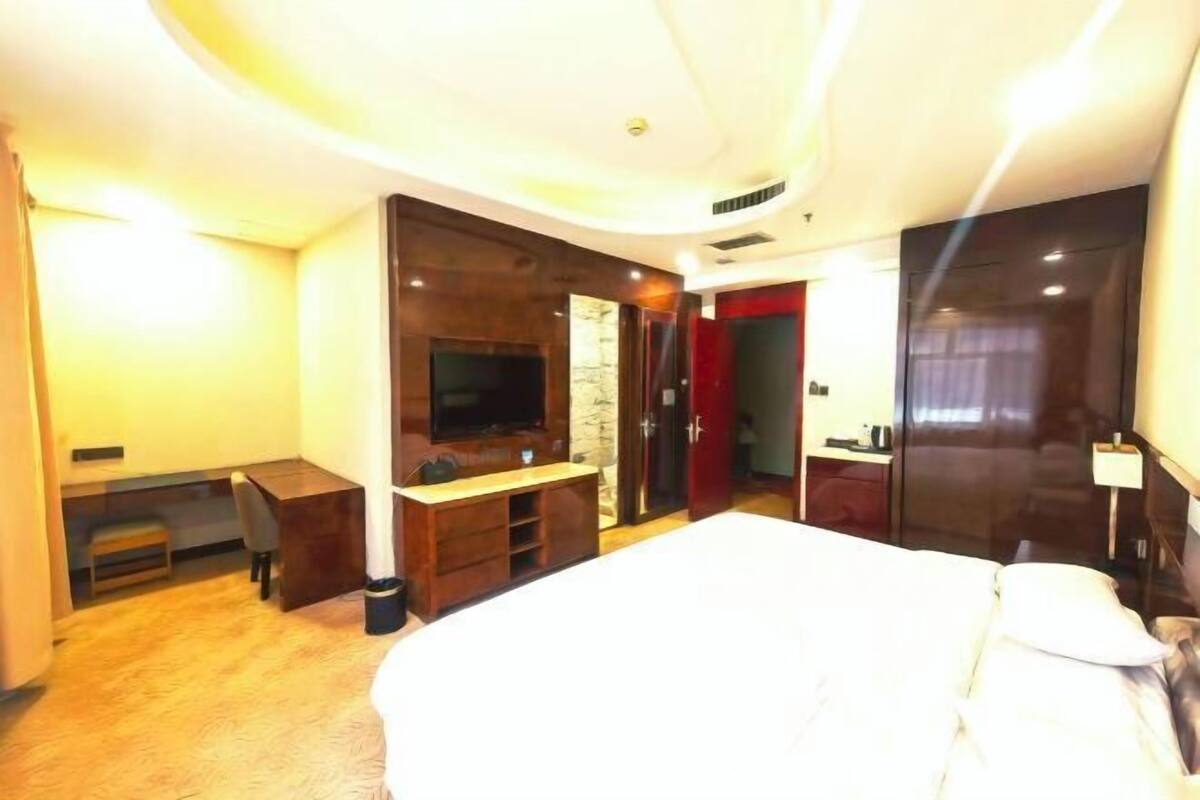 A hotel room with a large bed, a TV, a desk, and a wardrobe.