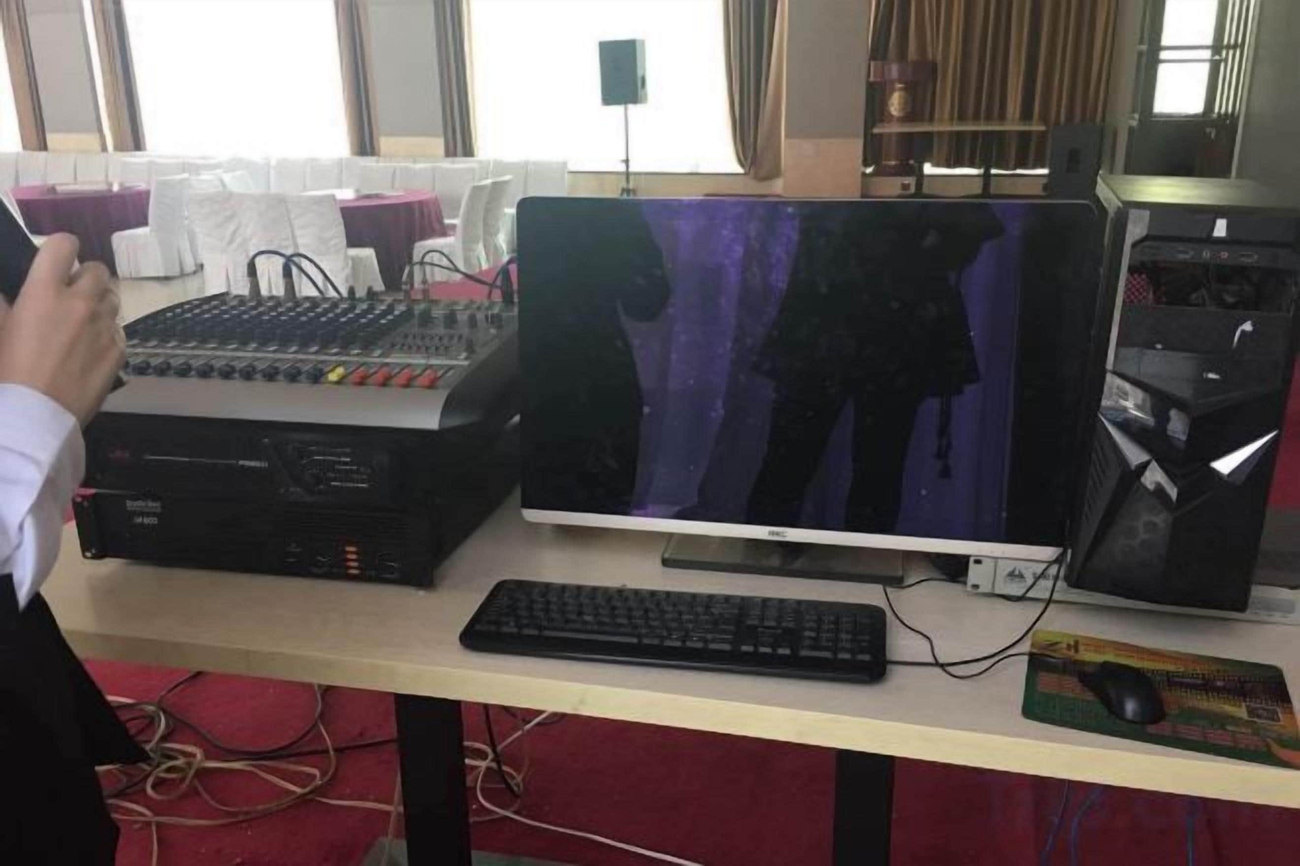 A computer setup with a mixer, monitor, keyboard, and mouse on a desk.