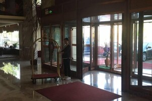 Un vestíbulo de hotel con una recepción, una puerta de vidrio de acceso y una alfombra roja que conduce a la entrada.